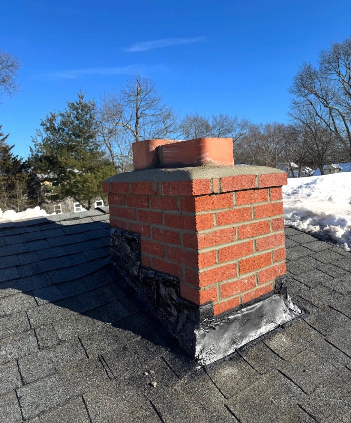 Brick chimney with new step flashing installed, snow on the roof